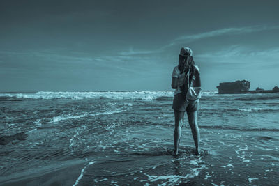Rear view of woman with backpack standing at shore against sky