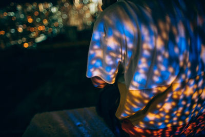 Lights reflecting on man sitting on retaining wall at night