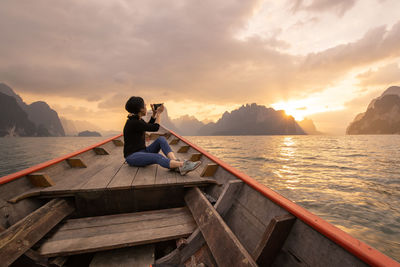 Man sitting on boat in sea against sky during sunset