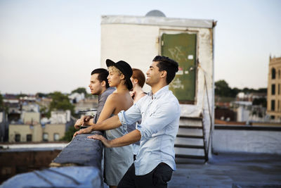 Happy friends enjoying at building terrace against clear sky