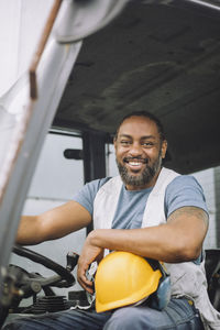 Portrait of happy mature construction worker with hardhat sitting in vehicle