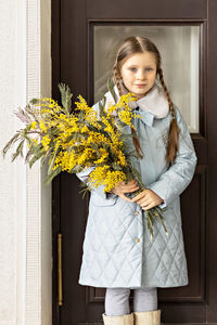 Portrait of a girl in a blue coat with a bouquet of mimosa in her hands in the park. spring