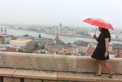 Full length of woman holding umbrella with hungarian parliament building in background