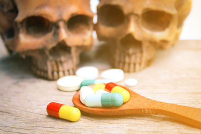 Close-up of wooden spoon with pills and human skulls on table