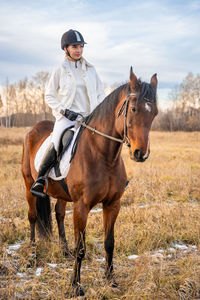 Side view of man riding horse on field against sky