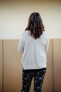 Rear view of woman standing against wall at home