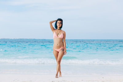 Full length of woman in bikini standing at beach against sky