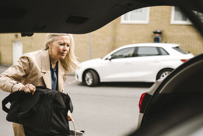 Blond businesswoman loading luggage in car trunk