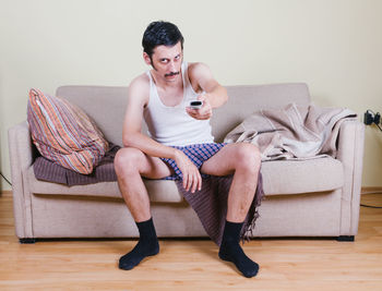 Portrait of mid adult man holding remote control while sitting on sofa at home