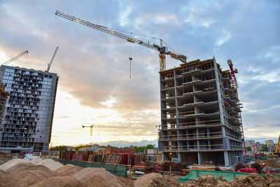 Low angle view of crane by building against sky