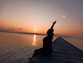 Silhouette person on pier by sea against sky during sunset
