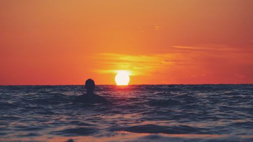 Silhouette person on sea against orange sky during sunset