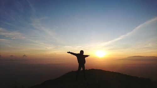 Rear view of silhouette man standing on mountain against sky during sunset
