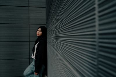 Portrait of a young woman standing against wall