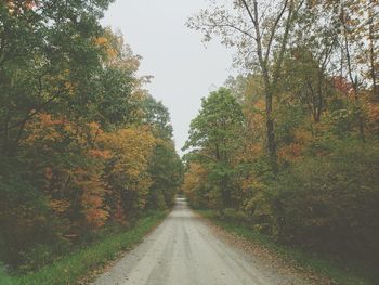 Road amidst trees against sky during autumn