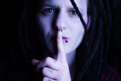 Close-up portrait of woman with finger on lips against black background