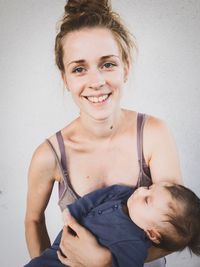 Portrait of smiling mother holding toddler daughter against wall