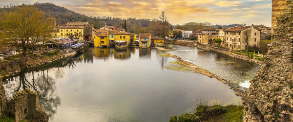  wide high angle view of borghetto sul mincio with the buildings reflecting on the water at sunset