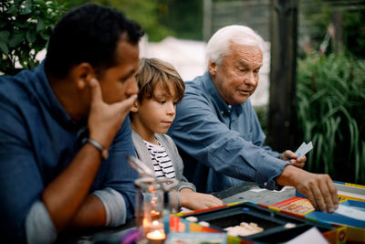 Multi-generation family playing board game while sitting at table in backyard