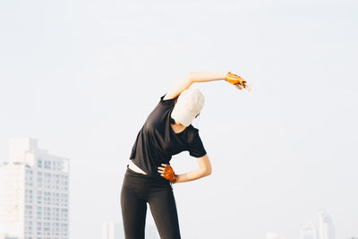 Young woman exercising while standing against clear sky