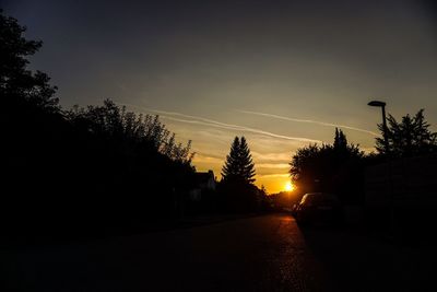 Silhouette trees by road against sky during sunset