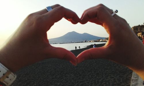 Midsection of man making heart shape against sea