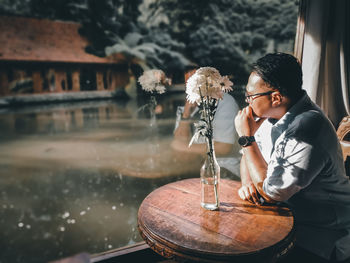 Man looking away while sitting by potted plant on table at cafe