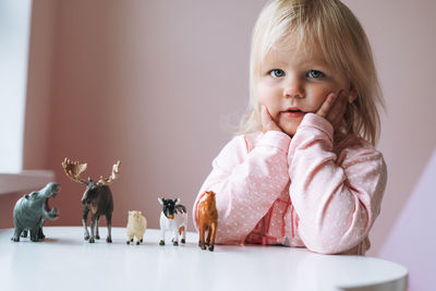 Little girl toddler in pink playing with animal toys on table in children's room at home