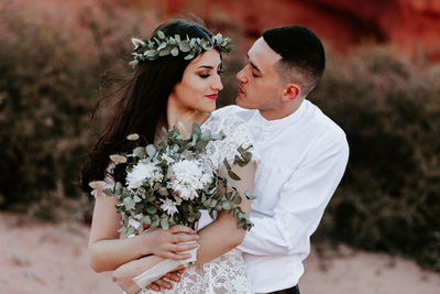 Beautiful young woman holding flower while standing by plant