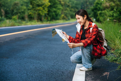 Young woman holding umbrella while sitting on road