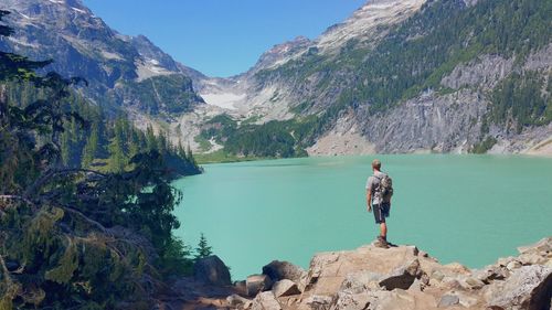 Full length of person standing on rock by lake against mountains