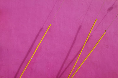 Yellow wires against pink wall during sunny day