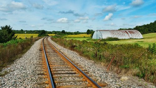 Railroad track by barn against sky