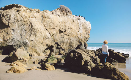 Rear view of woman standing on rock at beach