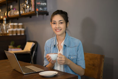 Portrait of smiling young woman using mobile phone at table