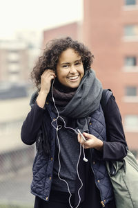 Portrait of happy female university student in warm clothing wearing headphones outdoors
