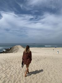 Rear view of woman on beach against sky