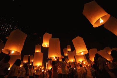 Low angle view of people releasing paper lanterns at night