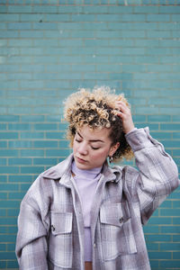 Young woman with hand in hair standing against wall