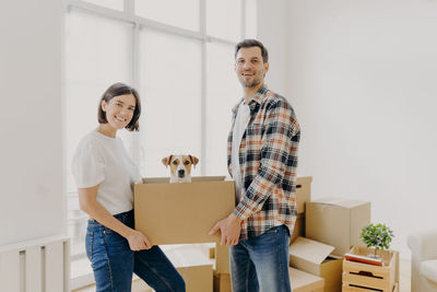 Portrait of smiling couple carrying puppy in box at home