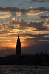 Scenic view of lake by silhouette buildings against sky during sunset