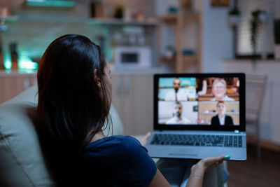 Rear view of woman using laptop at home