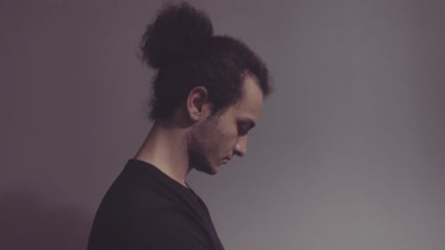 Young man looking down while standing against gray background