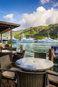 Chairs and tables at restaurant by sea by eden island, seychelles, against sky