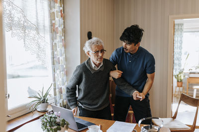 Male caregiver helping senior man while standing up at home