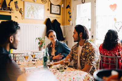 Smiling young woman with male friends while sitting at table in restaurant