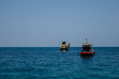 Fishing boats in sea against clear sky