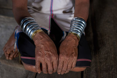 Low section of senior woman wearing bangles while sitting on wooden floor