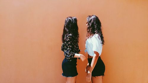 Side view of women standing against brown wall