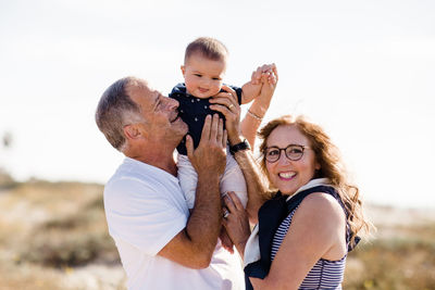 Grandparents smiling & holding grandson on beach